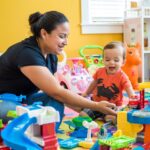 Professional nanny engaging a toddler in educational play activities at home.