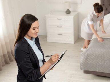 Household manager checking a task list while a housekeeper prepares a bedroom.