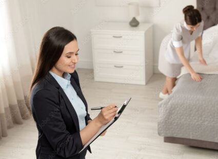 Household manager checking a task list while a housekeeper prepares a bedroom.