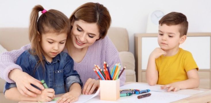 Professional nanny helping children with creative learning activities at home in Mumbai.